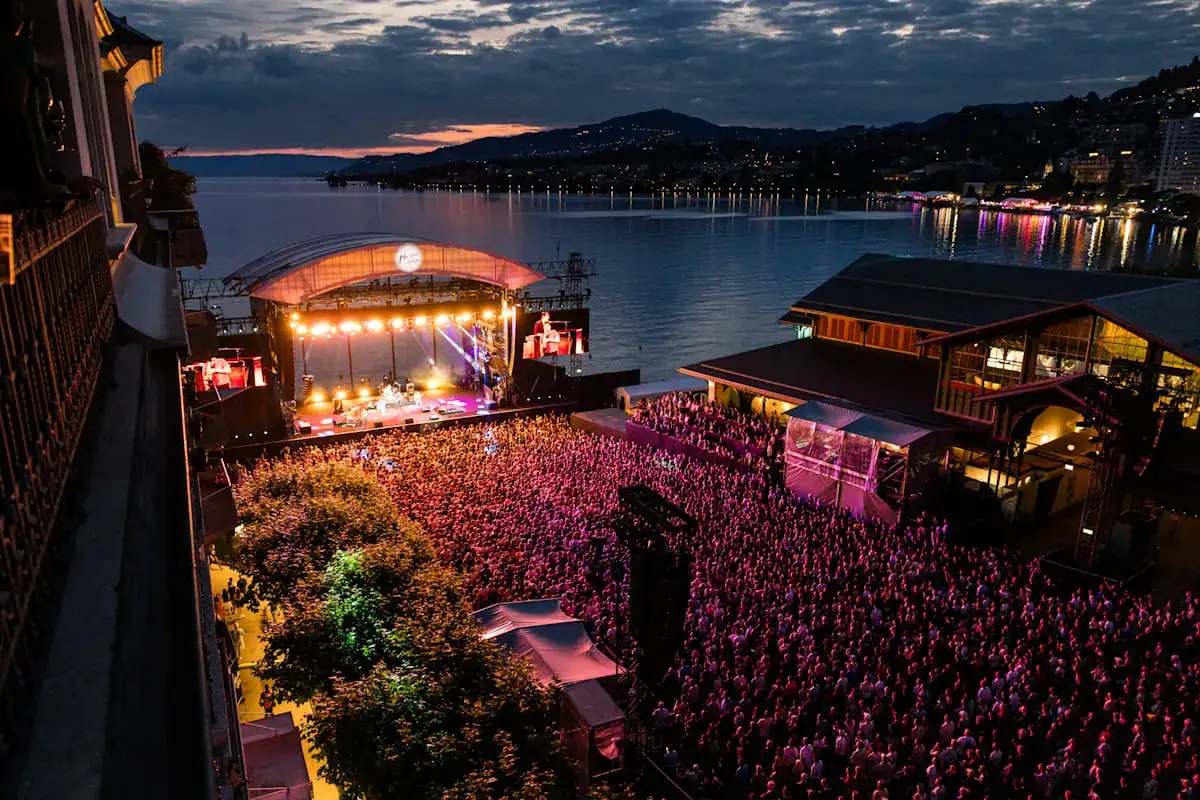 Ein riesiges Publikum feiert beim Jazz Montreux ein Konzert am Seeufer. Lichter spiegeln sich im Wasser.