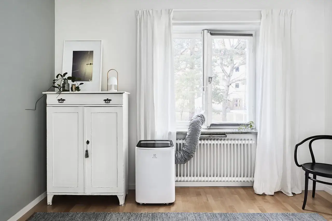Un climatiseur Electrolux portable, avec son tuyau d'évacuation dirigé vers la fenêtre, assure une fraîcheur bienvenue dans ce salon lumineux.