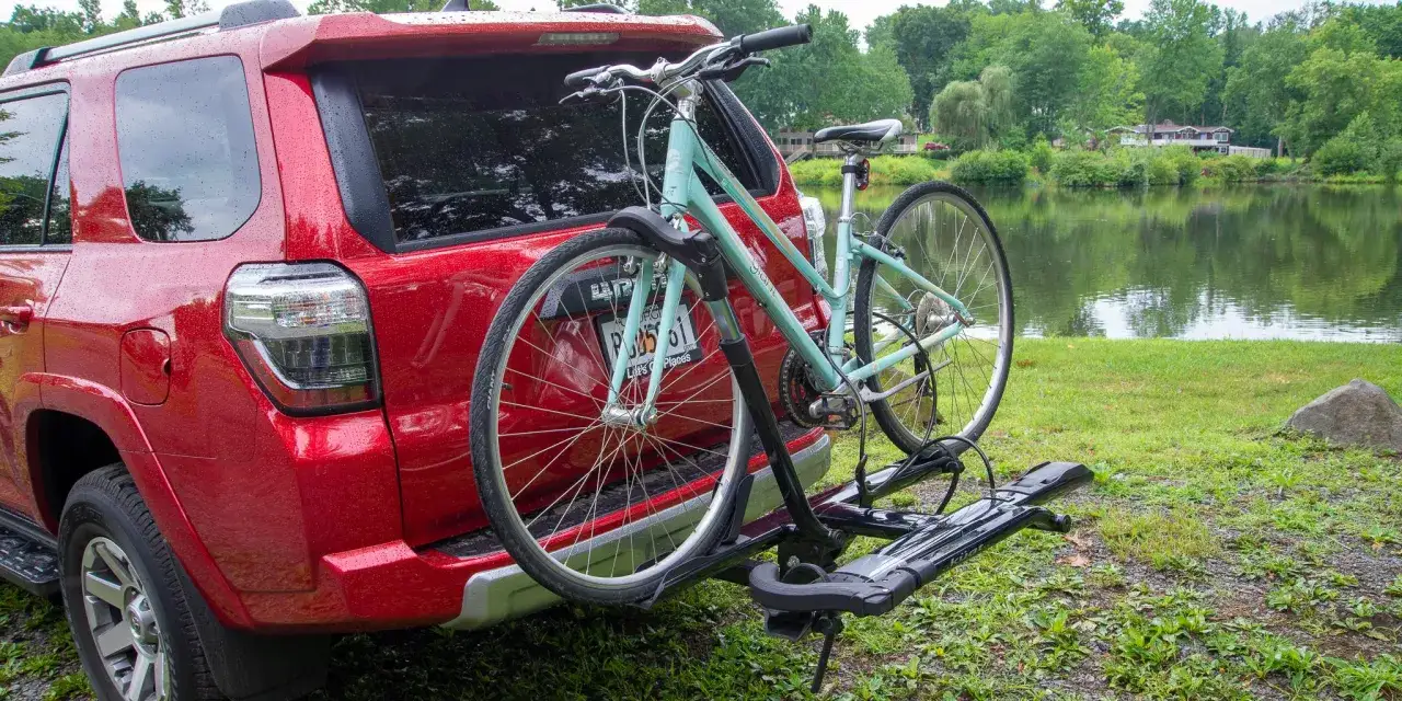 R&ouml;d bil med cykelst&auml;ll och en ljusbl&aring; cykel redo f&ouml;r &auml;ventyr vid en sj&ouml;. Perfekt f&ouml;r att frakta cykeln till nya platser.