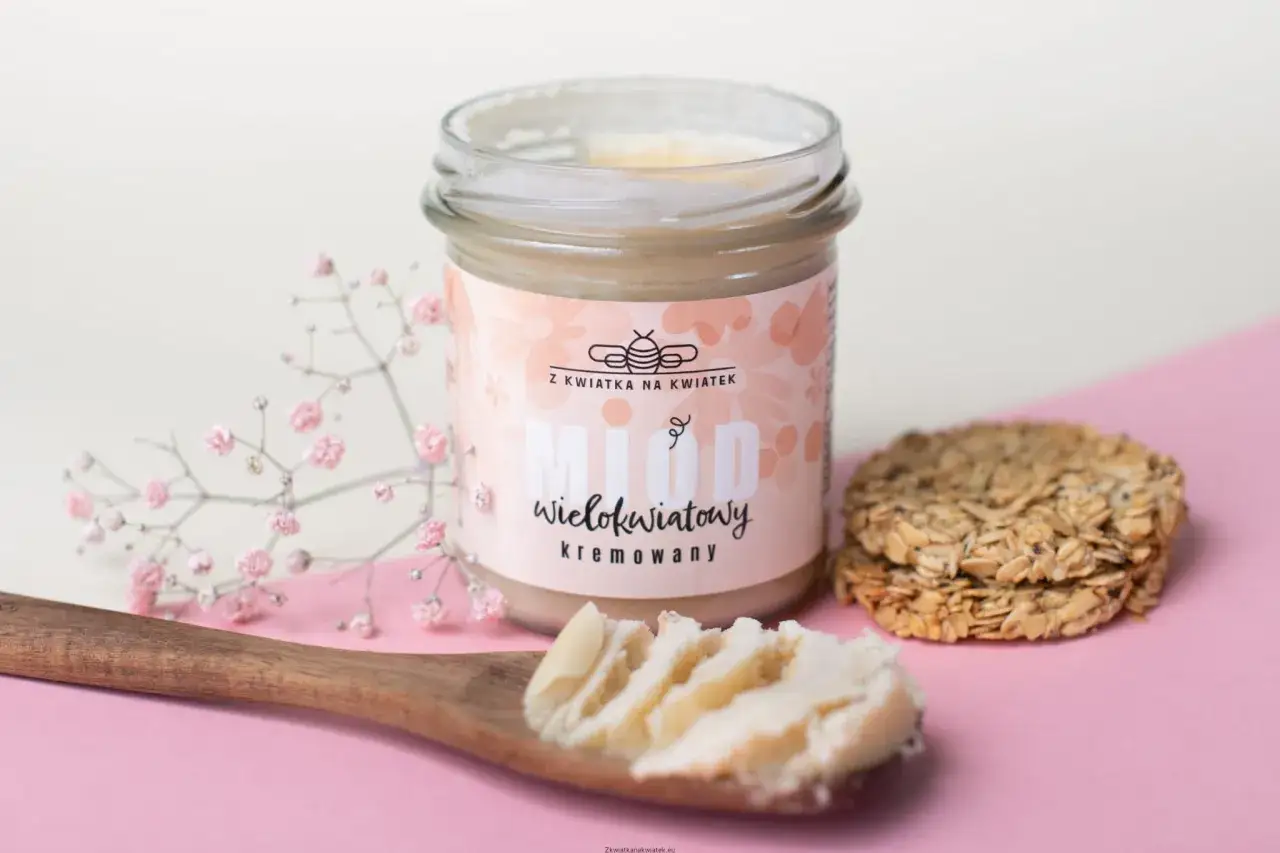 Słoik miodu wielokwiatowego kremowanego, z drewnianą łyżką pełną miodu i ciasteczkami owsianymi. Brak wad w tym naturalnym produkcie.
