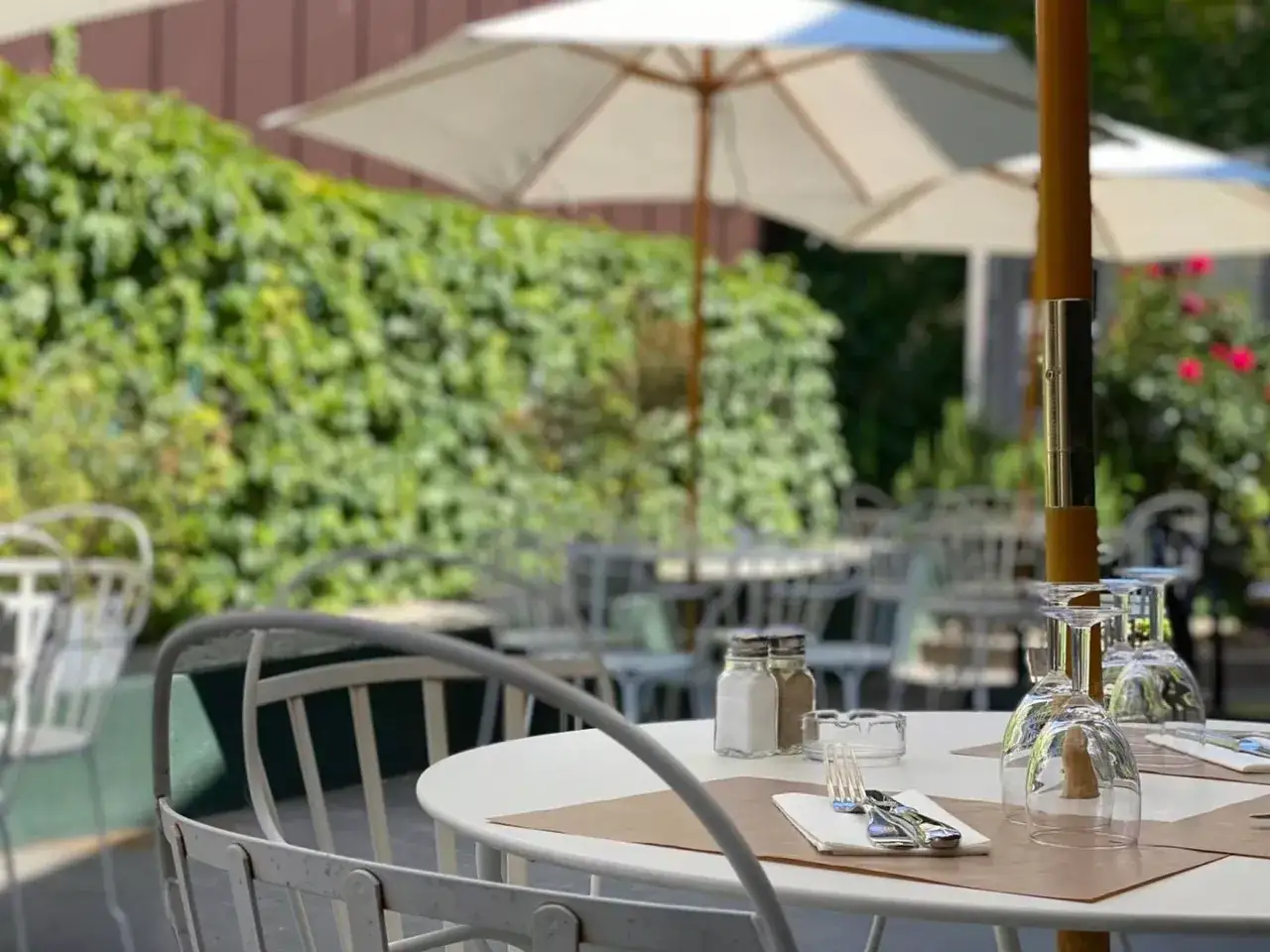 Terrasse d'un restaurant à Aurillac, ouvert le dimanche. Tables dressées sous des parasols, entourées de verdure.