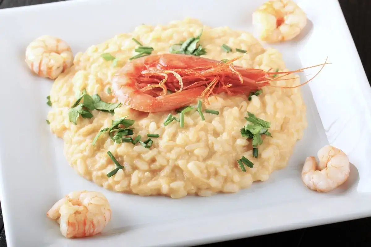 Un cremoso risotto alla crema di scampi, guarnito con scampi freschi e erbe aromatiche, servito su un piatto bianco.