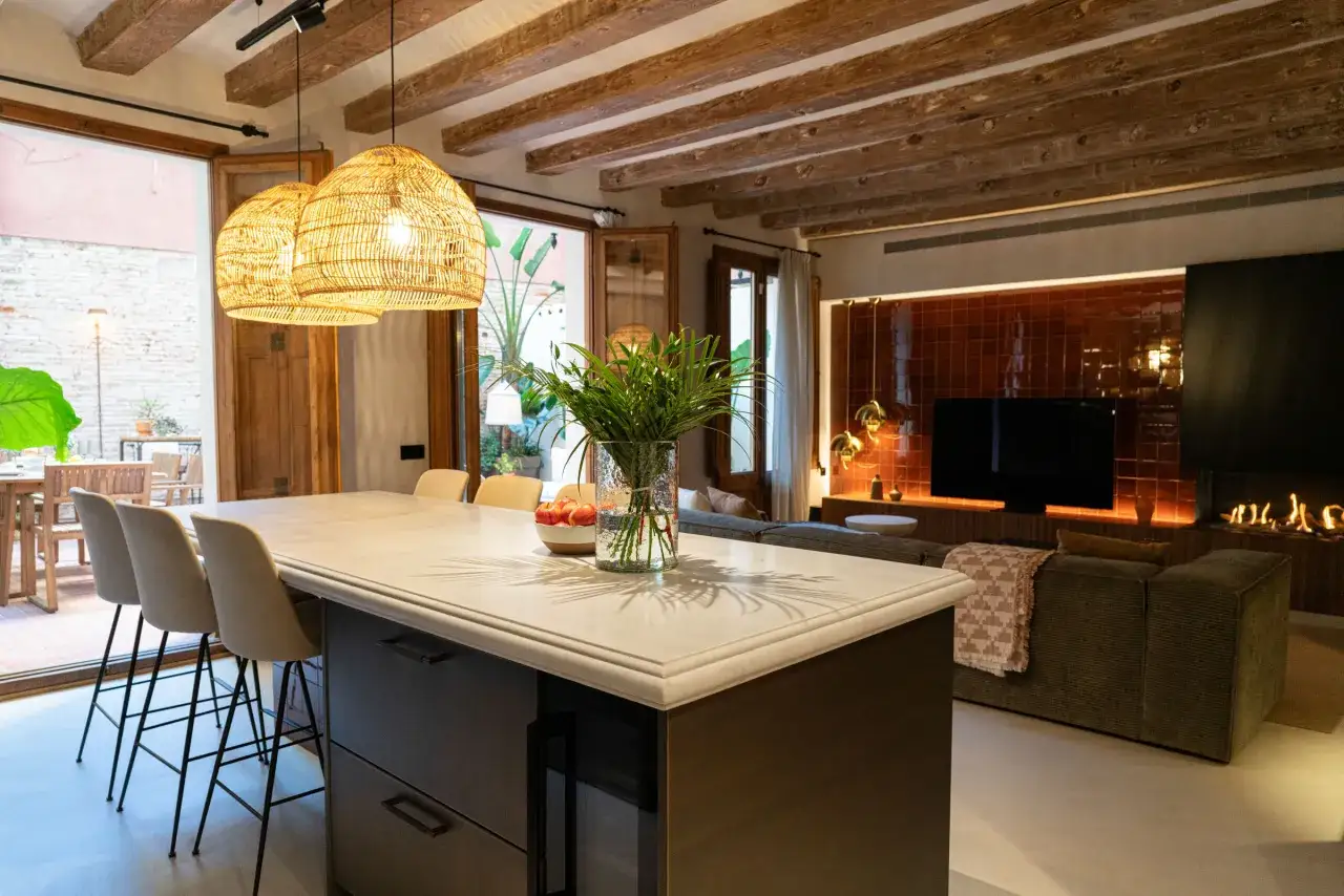Cocina y salón integrados, creando un espacio diáfano. La isla de cocina se une visualmente al salón con chimenea y sofás.