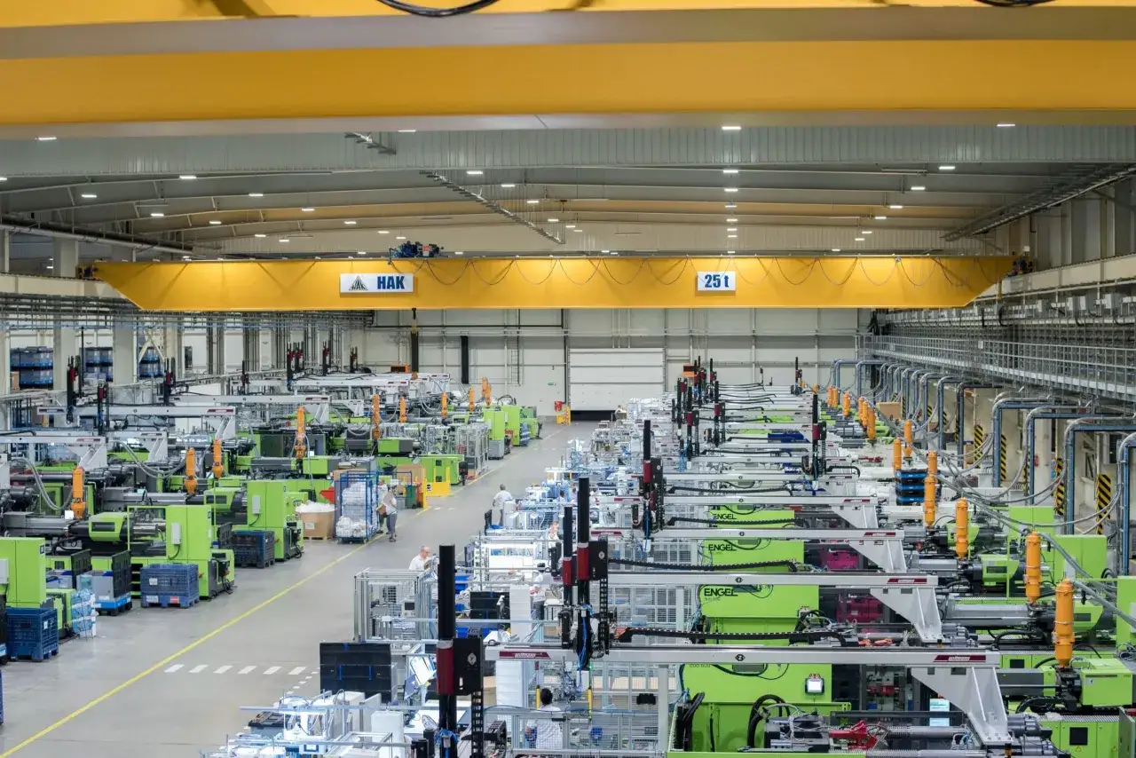 Nowoczesna hala produkcyjna z rzędami zielonych maszyn, gdzie zaawansowana technologia produkcji zapewnia wydajność. Żuraw HAK o udźwigu 25t nadzoruje proces.
