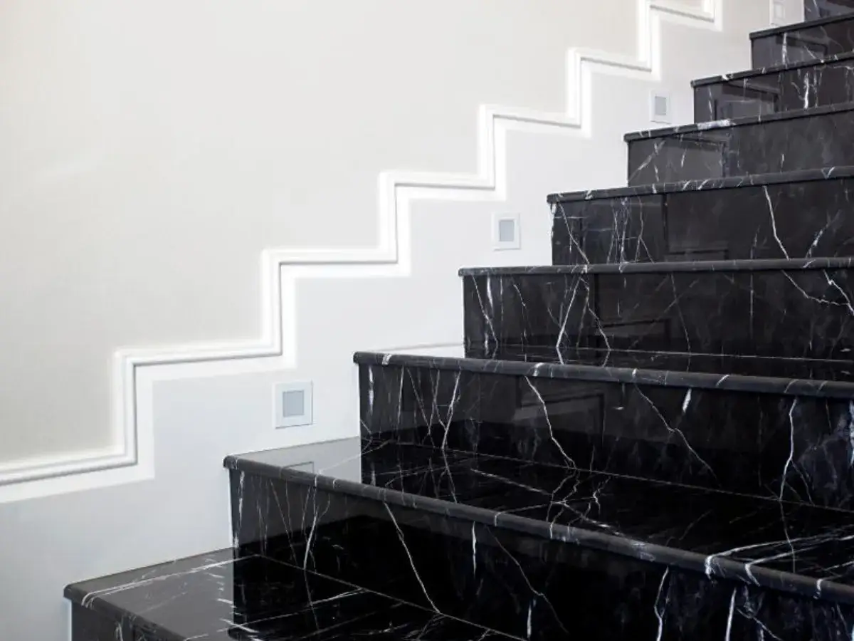 Scala interna in marmo nero lucido con venature bianche, illuminata da faretti e profili luminosi. Un modo elegante per abbellire una scala interna.