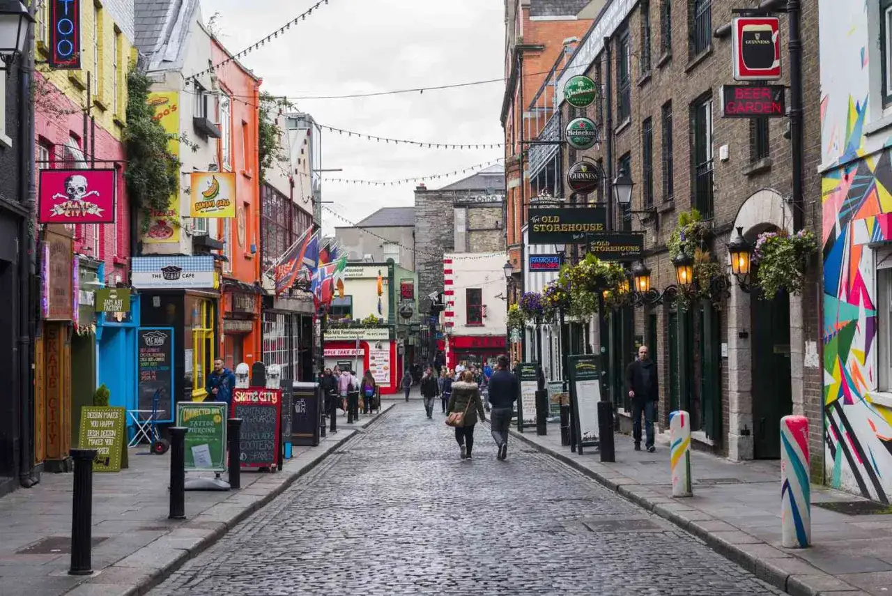 En kullerstensbelagd gränd i Dublin med färgglada fasader, skyltar för pubar som 