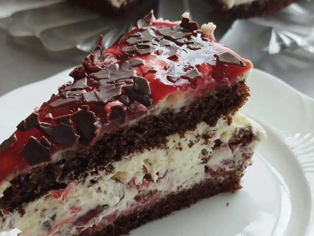 Ein Stück Schokoladenkuchen mit Kirschen und Sahne, garniert mit Schokostreuseln und roter Glasur. Diese Stracciatella Torte sieht köstlich aus.