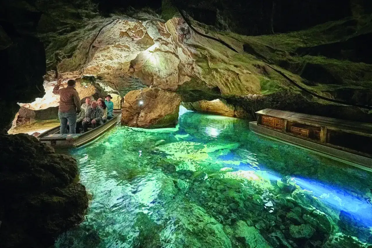 Bootsfahrt durch die Höhle der Zwiefalter Aach. Besucher bestaunen das smaragdgrüne Wasser und die Felsformationen.