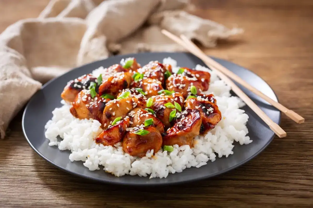 Pyszna wieprzowina teriyaki z sezamem i szczypiorkiem na białym ryżu, gotowa do jedzenia pałeczkami.