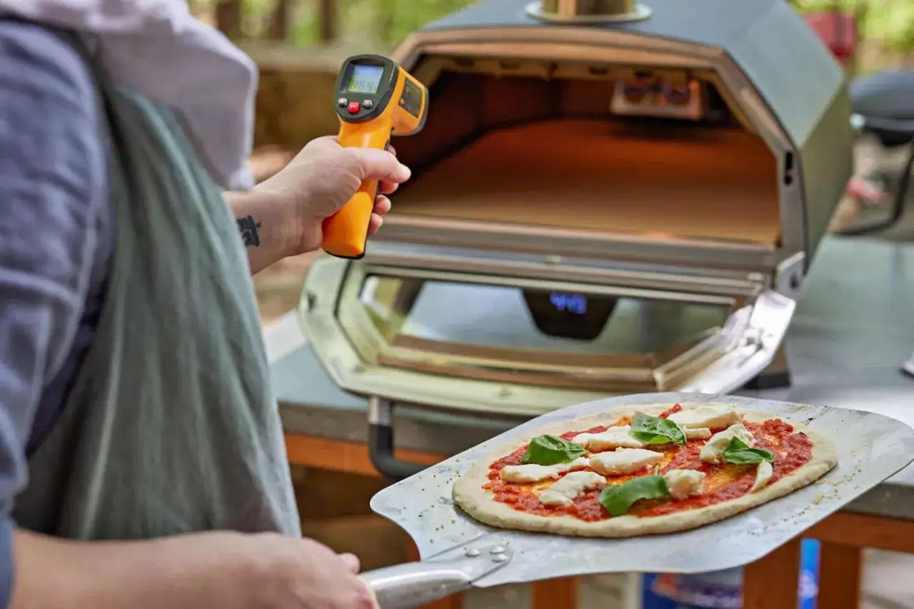 Sprawdzanie temperatury pieca do pizzy na kamieniu. Na łopacie czeka pizza z mozzarellą i bazylią.