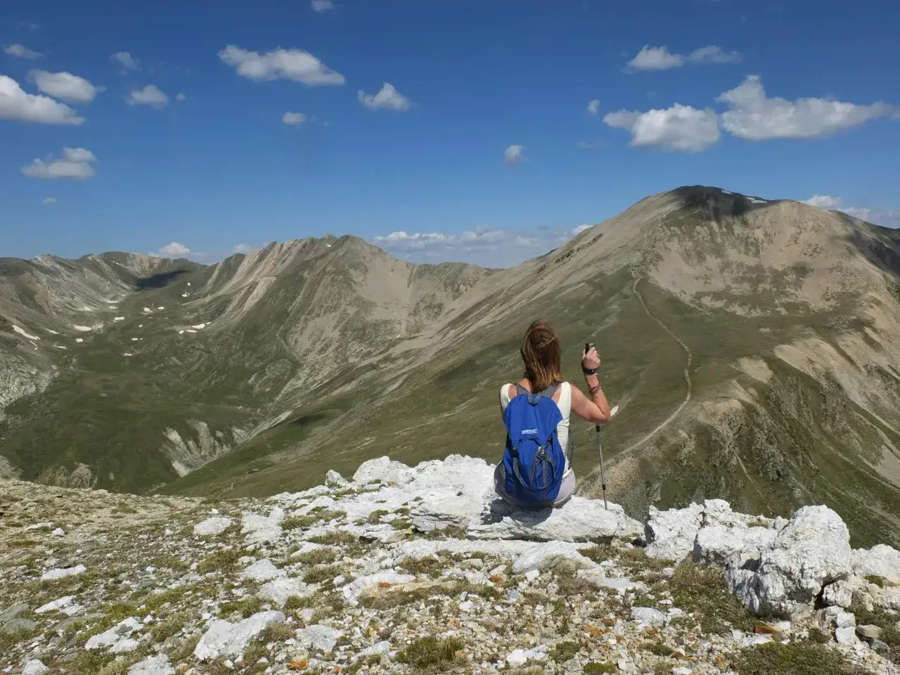 Kobieta z plecakiem i kijkami trekkingowymi odpoczywa na szczycie, podziwiając malowniczą trasę na samotnie.