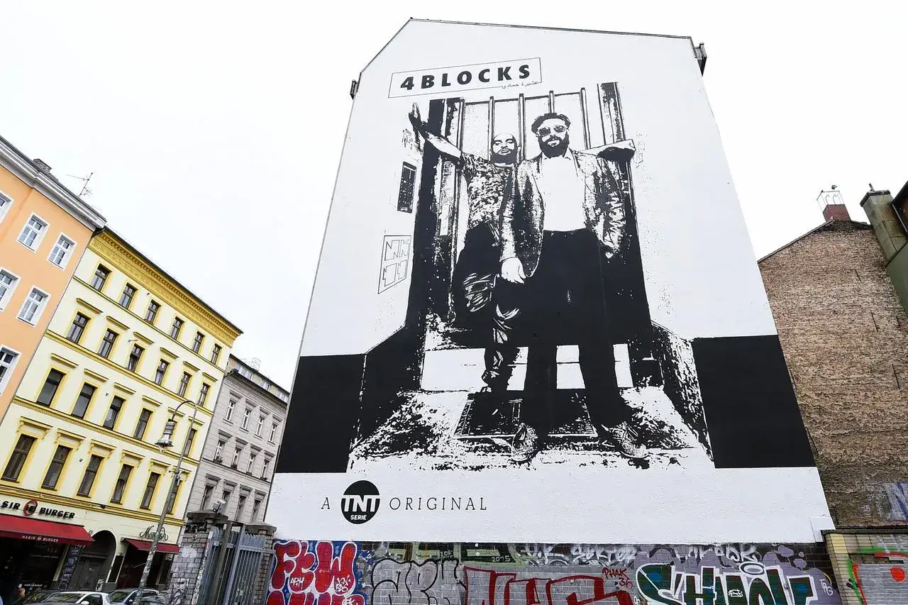 Gro&szlig;es Wandbild mit zwei M&auml;nnern, die vor Gittern stehen. &Uuml;ber ihnen steht 