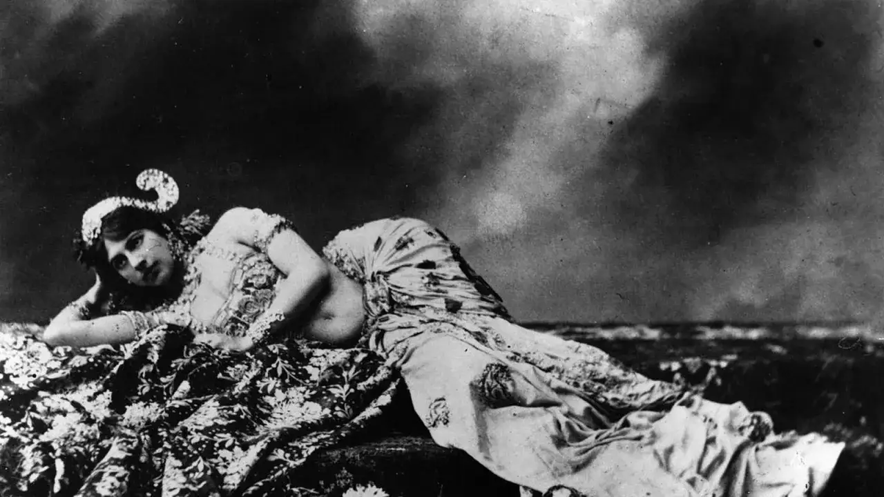 Mata Hari, la ex&oacute;tica bailarina, yace recostada sobre telas estampadas, con un tocado adornado y mirada seductora.
