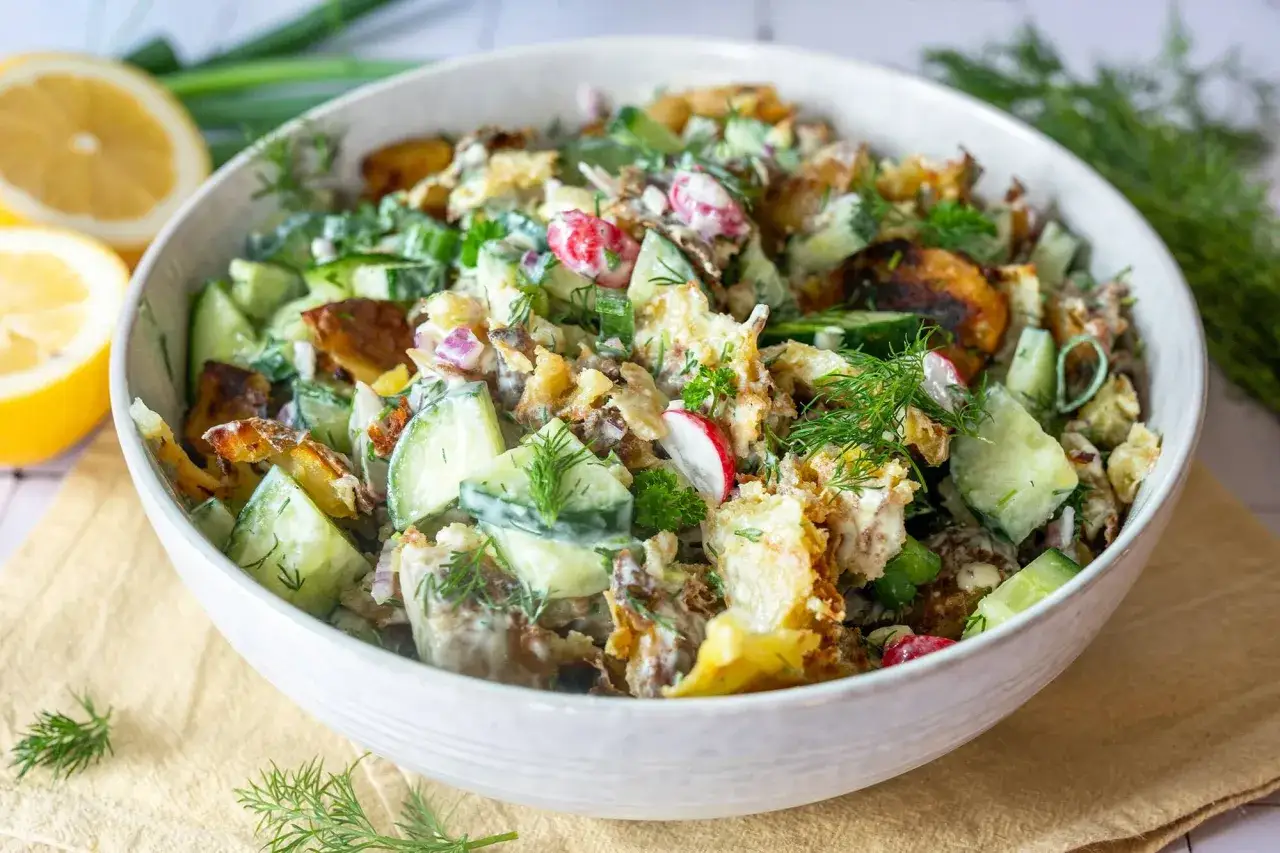 Herzhafter smashed potato salat mit Gurken, Radieschen und Dill in einer Schüssel, garniert mit Zitrone.