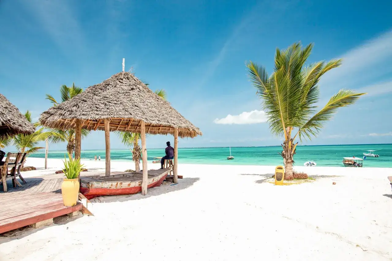 Rajska plaża na Zanzibarze z palmami i łodzią. Sprawdź aktualne Zanzibar ceny, by zaplanować wymarzone wakacje.