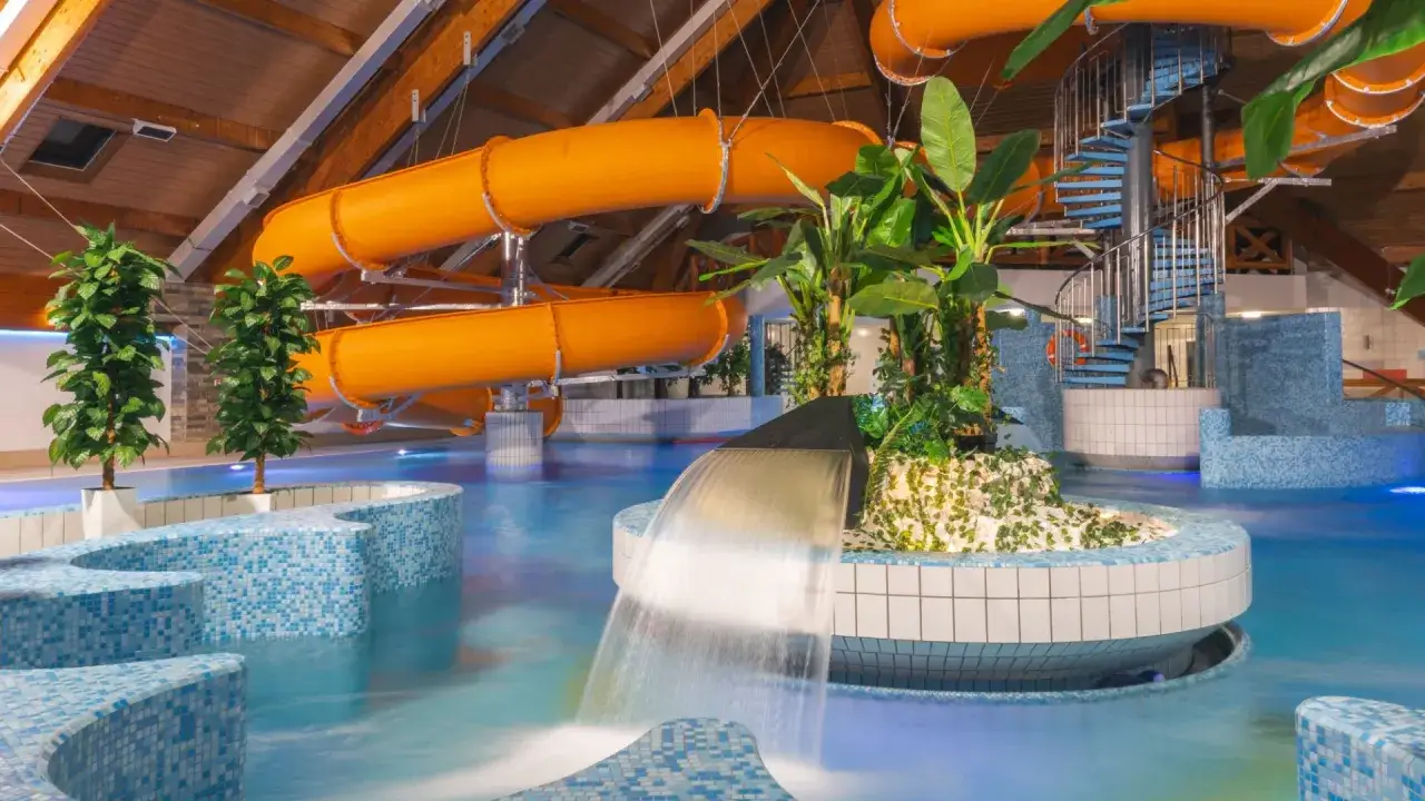 Wesoły hotel z aquaparkiem dla dzieci w górach. Pomarańczowe zjeżdżalnie, basen i tropikalna roślinność tworzą raj dla maluchów.