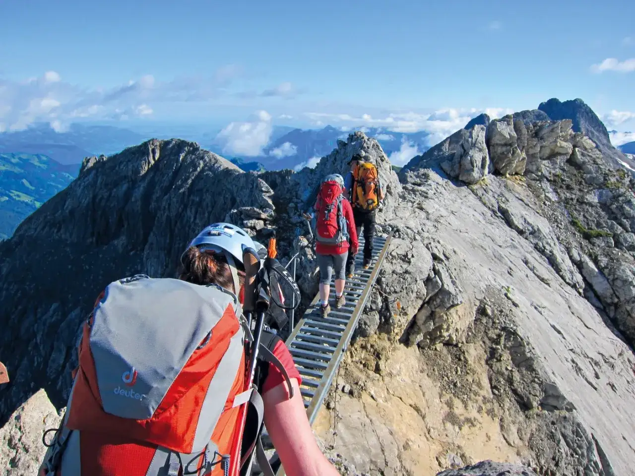Drei Wanderer auf einem schmalen Steig mit Klettersteig-Elementen in den Alpen. Perfekt für abenteuerliche 5-Tage-Wandertouren.