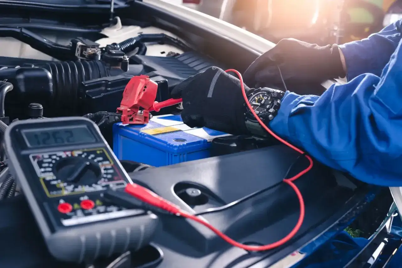 Mechanik w rękawiczkach dokonuje kodowania akumulatora, używając multimetru do sprawdzenia napięcia.