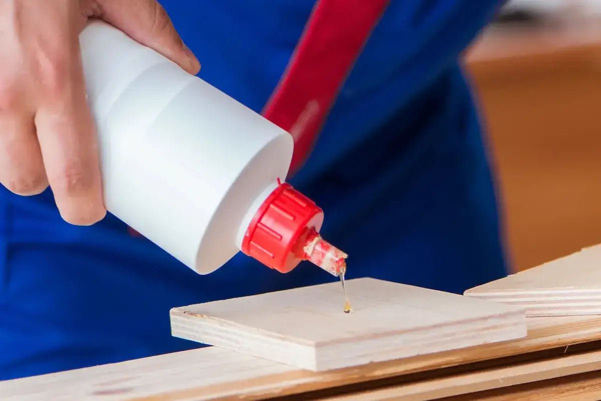Application de colle sur bois. Une goutte de colle bi-composant tombe d'une bouteille blanche sur une pi&egrave;ce de bois.