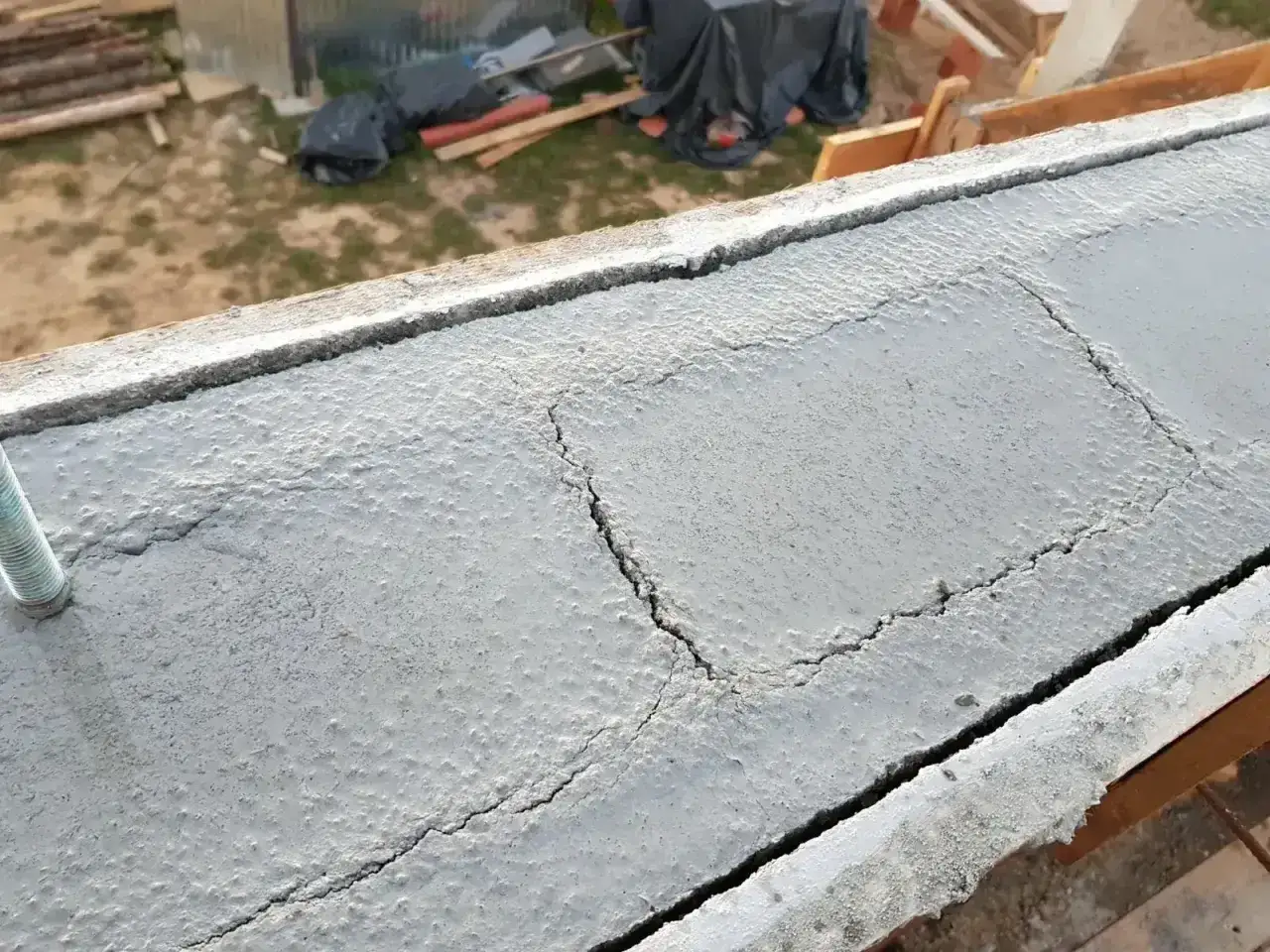 Pęknięcia na świeżym betonie, który miał być częścią wieńca budowlanego. Widać śruby kotwiące.