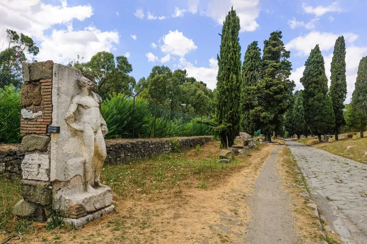 Vestige de la via antica Roma, une statue antique se dresse pr&egrave;s d'une route pav&eacute;e bord&eacute;e de cypr&egrave;s.