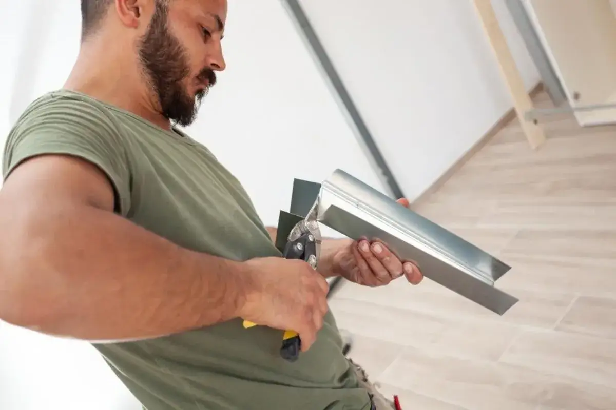 Un homme coupe un rail de placo avec des cisailles. Il prépare le matériau pour une installation.