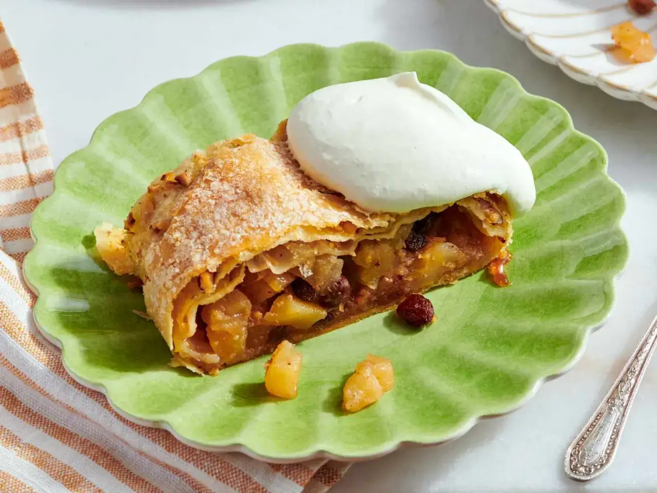 Un trozo de strudel de manzana, con su masa dorada y relleno de fruta, coronado con una generosa porción de nata montada.