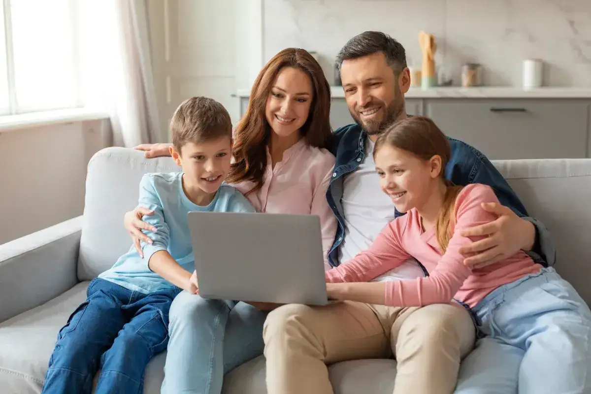 Rodzina ogląda coś na laptopie, śmiejąc się. Dzieci siedzą na kolanach rodziców. To wspaniałe chwile, warte 1000 plus.