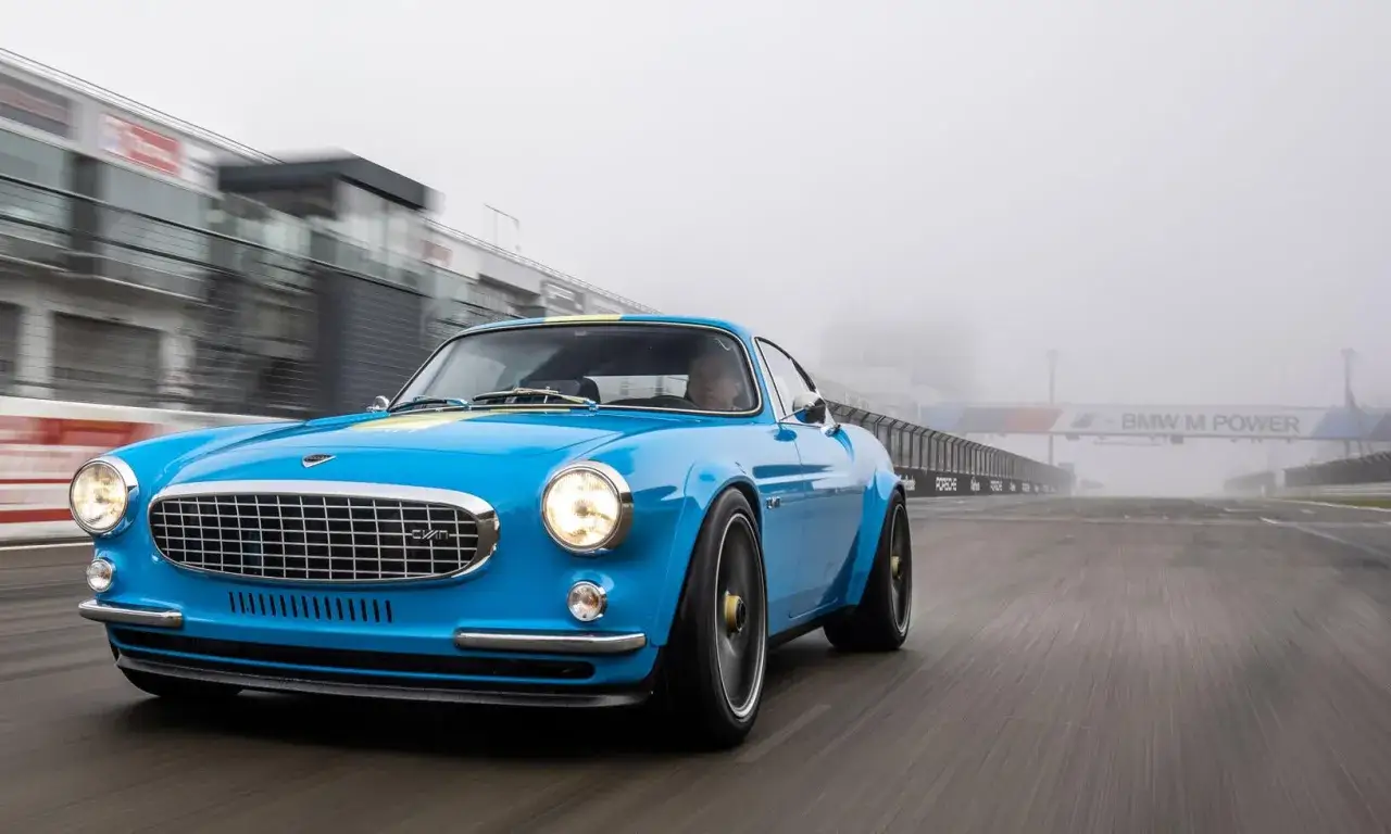 En blå Volvo P1800, en moderniserad klassiker, kör på en dimmig racerbanan. Denna 