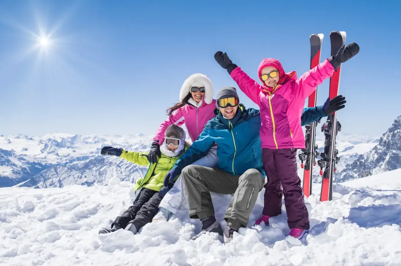 Famille heureuse profitant des sports neige en montagne, sous un soleil éclatant.
