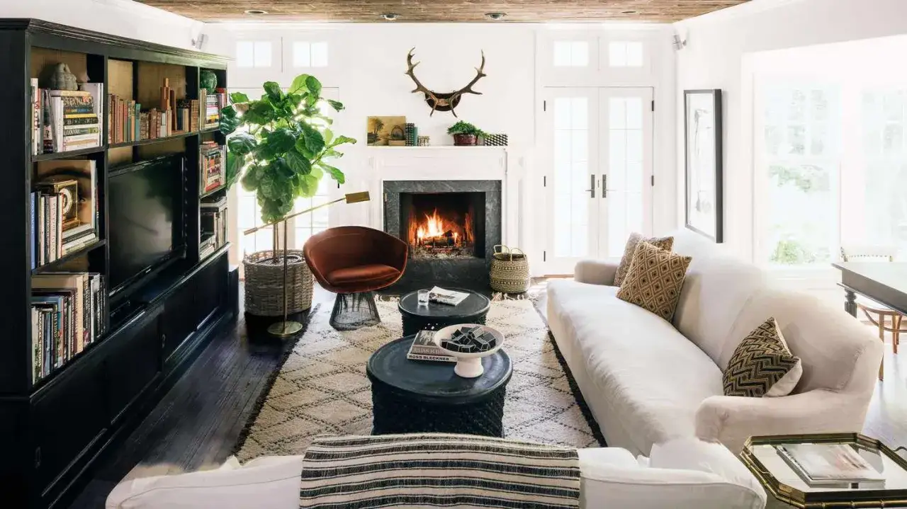 Un salon cosy avec un feu de chemin&eacute;e cr&eacute;pitant, un canap&eacute; blanc invitant, une biblioth&egrave;que remplie et une plante luxuriante.