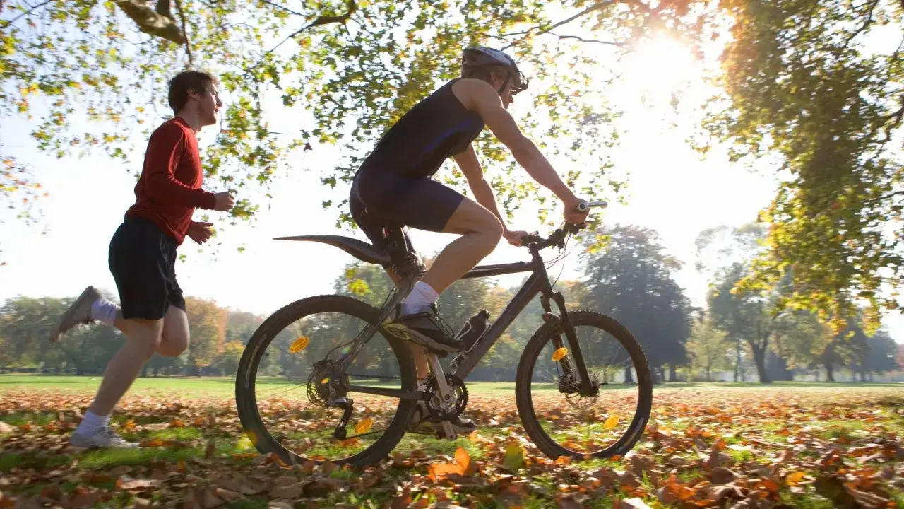 Uomo in bicicletta e un corridore in un parco autunnale, allenamento per come migliorare la resistenza.