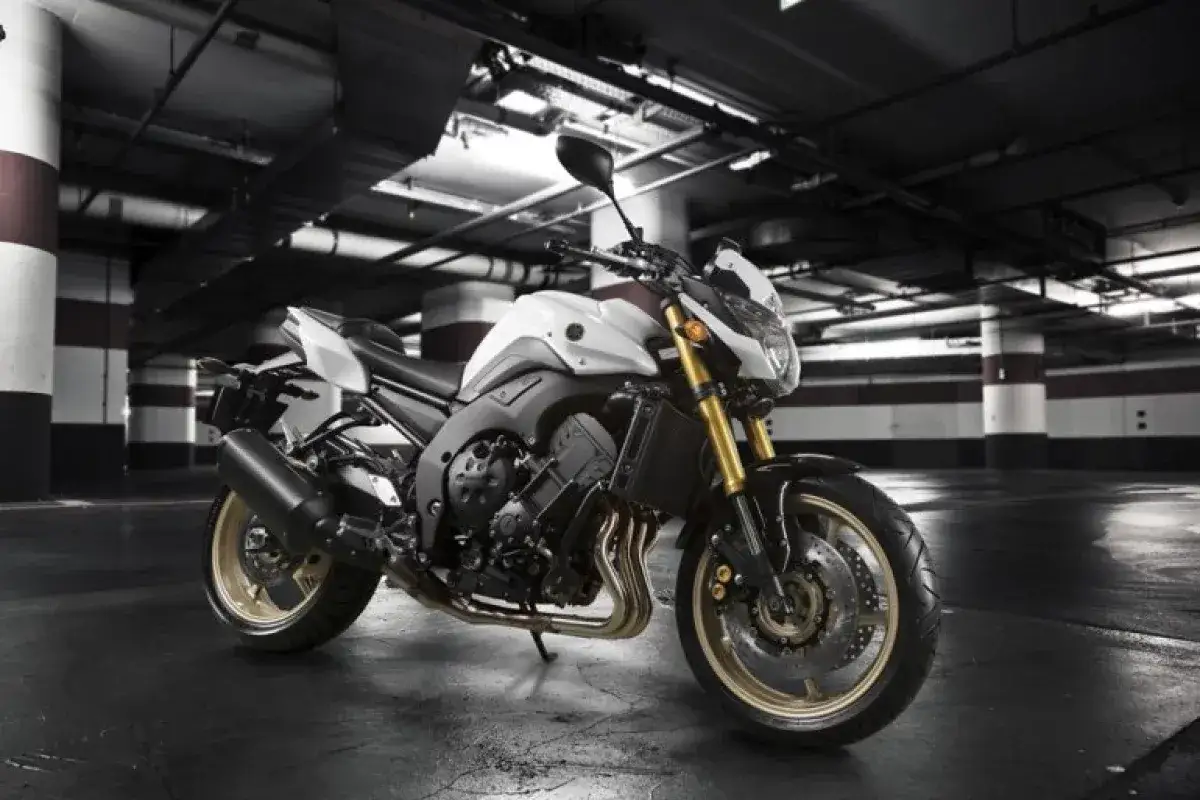 Biały motocykl Yamaha FZ8N z detalami w kolorze złotym i czarnym, zaparkowany w podziemnym garażu.