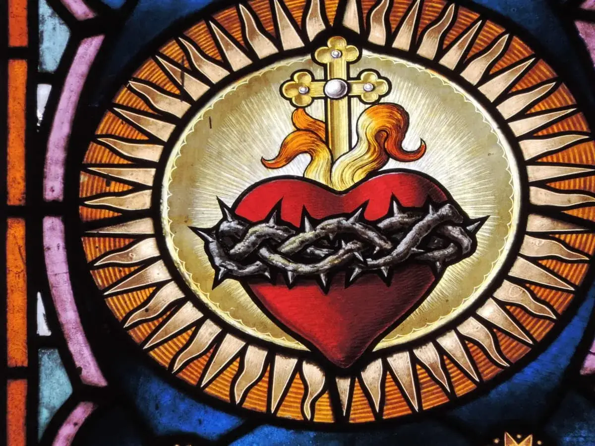 Witraż przedstawia symbol serca otoczonego cierniową koroną, krzyżem i płomieniami. To symbol miłości i ofiary.