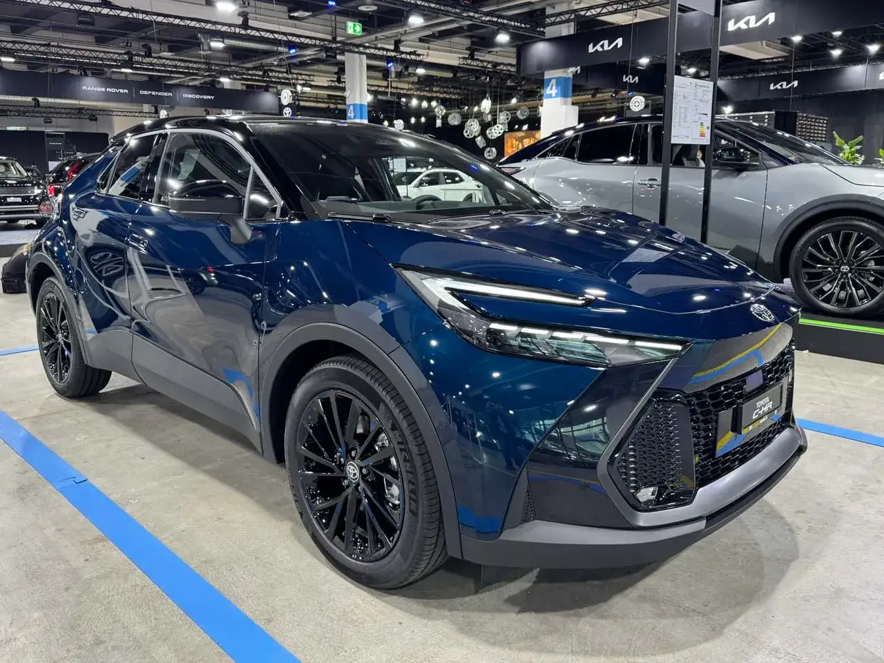 Nowy, ciemnoniebieski Toyota C-HR 2025 błyszczy na wystawie, prezentując swój futurystyczny design i czarne felgi.
