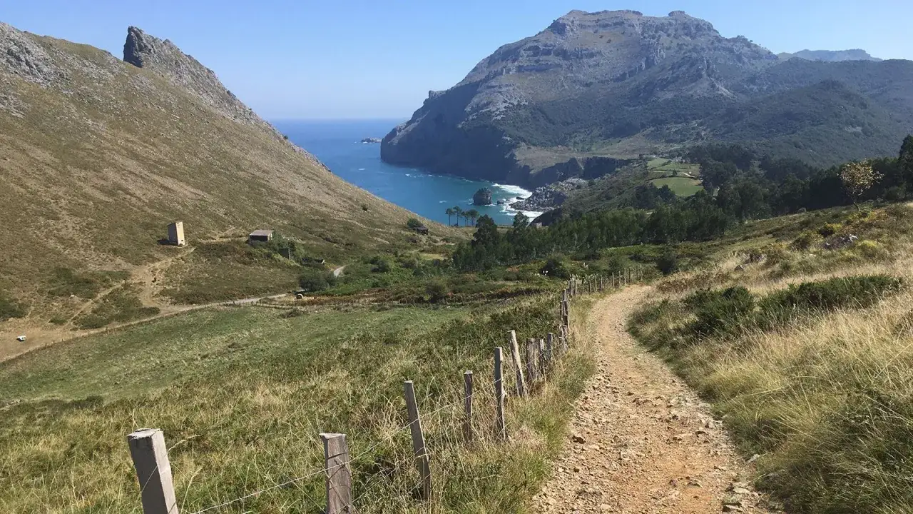 Ein schmaler Pfad f&uuml;hrt durch gr&uuml;ne H&uuml;gel zum Meer. Der Jakobsweg Nordspanien verspricht atemberaubende Ausblicke und einsame Wege.