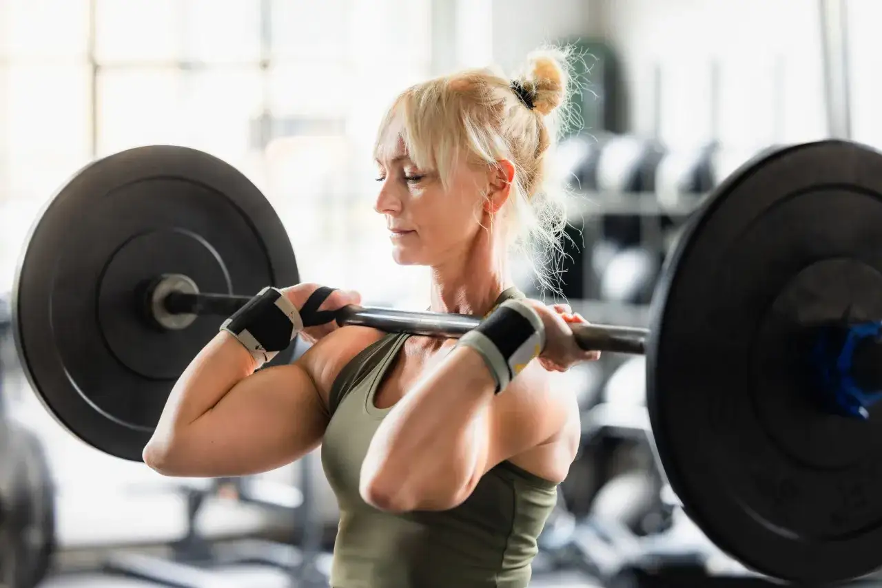 Stark kvinna med blont hår i knut lyfter skivstång. Hon tränar enligt madcow 5x5.
