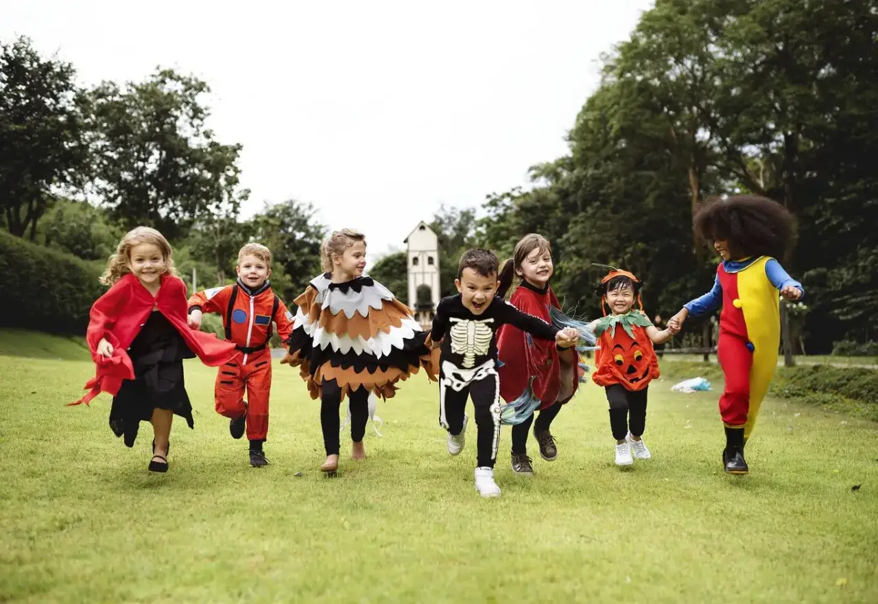 Niños corriendo en disfraces de carnaval: astronauta, búho, esqueleto, calabaza y payaso. ¡Pura alegría!