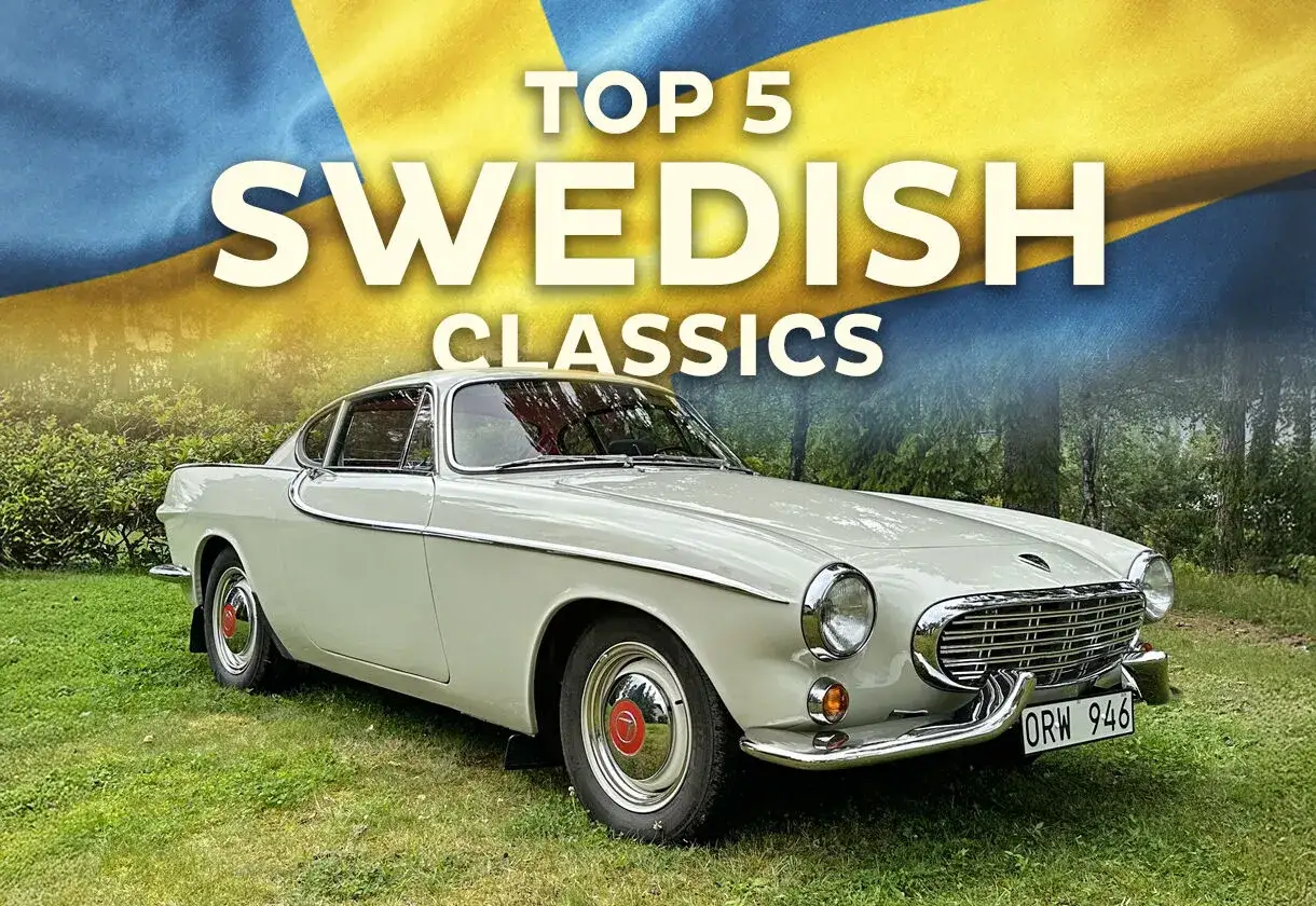 En vit Volvo P1800 från 60-talet står på en gräsmatta framför en svensk flagga. En klassisk svensk bil.