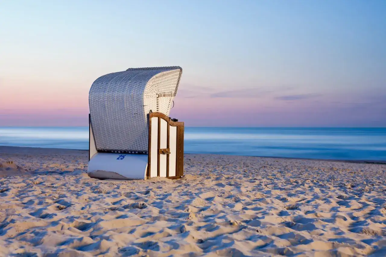 Pusta plaża z koszem plażowym, idealna dla małych miejscowości nad morzem. Delikatne kolory zachodu słońca nad spokojnym morzem.