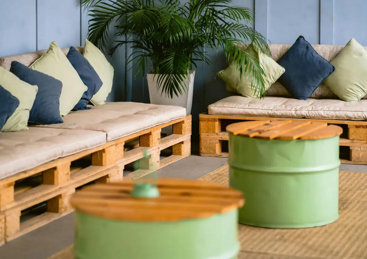 Sofás y mesas bajas creados con **decoración con palets**, complementados con cojines y plantas para un ambiente acogedor.