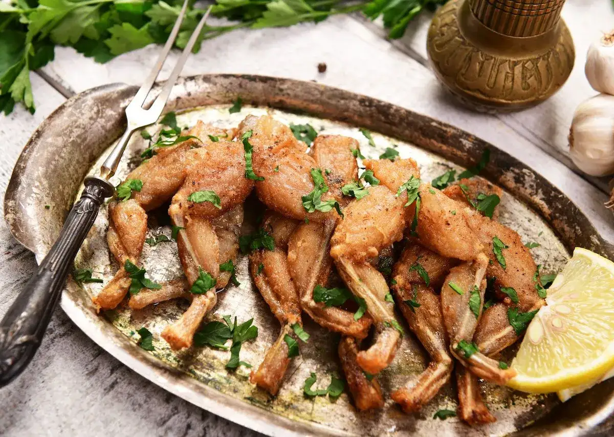 Ancas de rana receta francesa, doradas y crujientes, servidas en bandeja de plata con perejil y lim&oacute;n.
