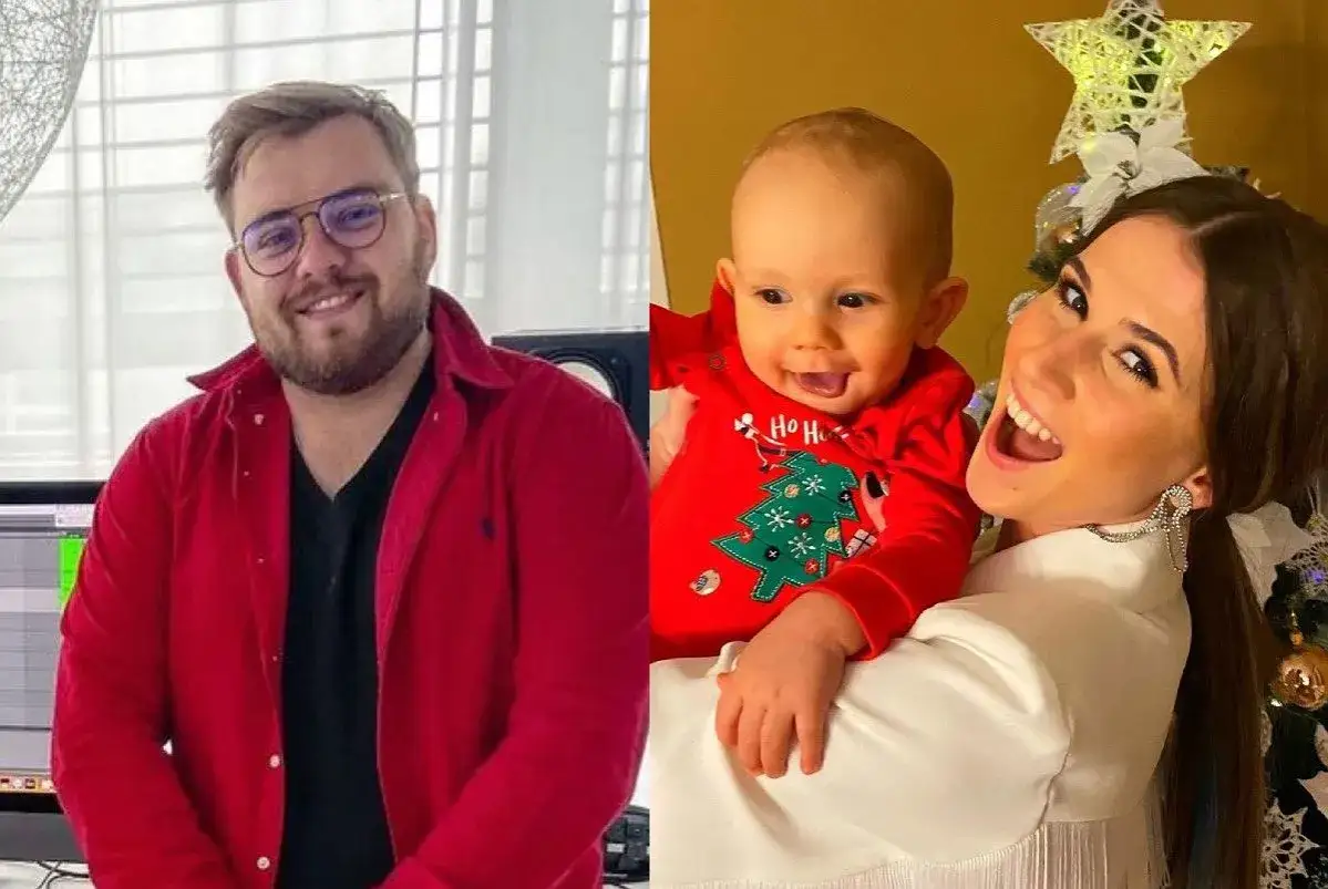 Kevin Mglej z dzieckiem w świątecznym body. Uśmiechnięta kobieta trzyma malucha na tle choinki.
