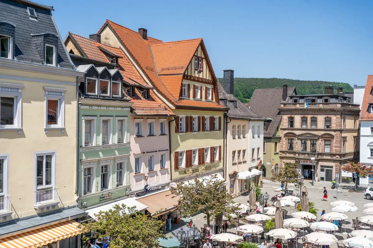Bunte H&auml;userfronten und ein belebter Platz mit Bierg&auml;rten pr&auml;gen die Kulmbach Altstadt. Sonnenschirme und Menschen beleben das Bild.