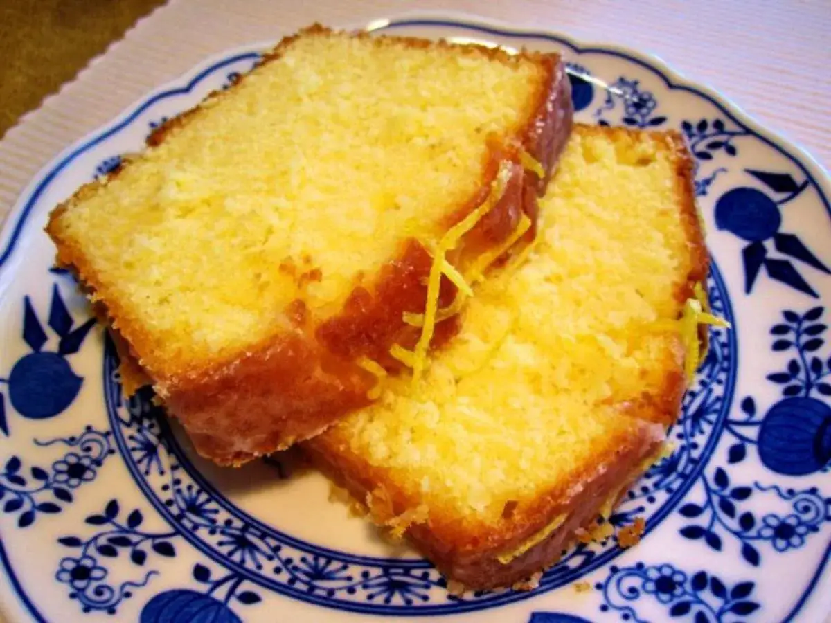 Zwei saftige Scheiben Zitronenkuchen aus der Kastenform, garniert mit Zitronenschale, auf einem blau-wei&szlig;en Teller.