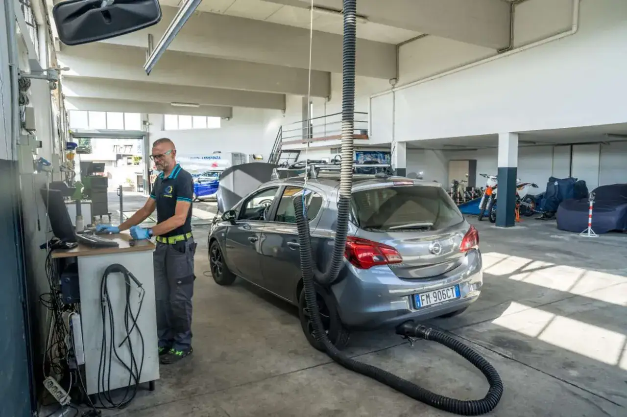 Tecnico effettua la prima revisione auto, collegando un tubo di scarico al computer per controlli.