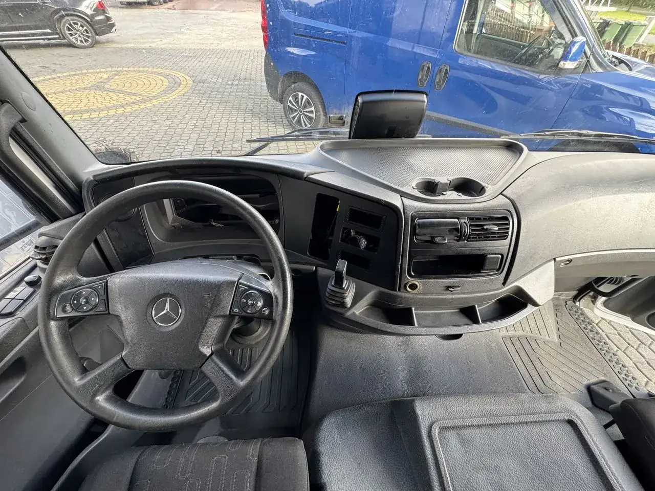 Wnętrze kabiny ciężarówki Mercedes Axor. Widok na kierownicę, deskę rozdzielczą i fotele.