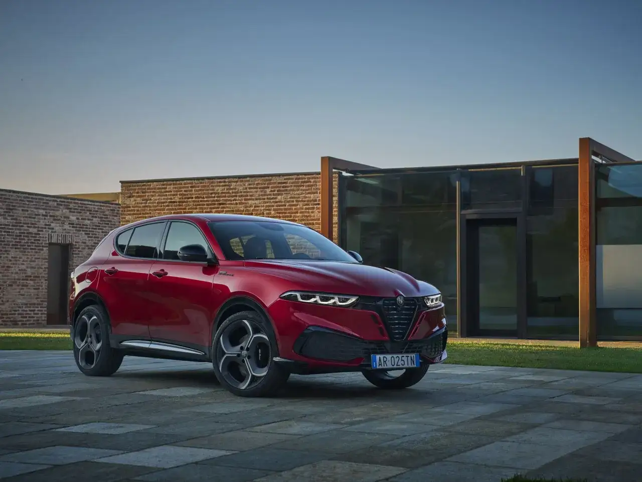 Roter Alfa Romeo Plug-in Hybrid steht vor einem modernen Gebäude mit Ziegel- und Glasfassade.
