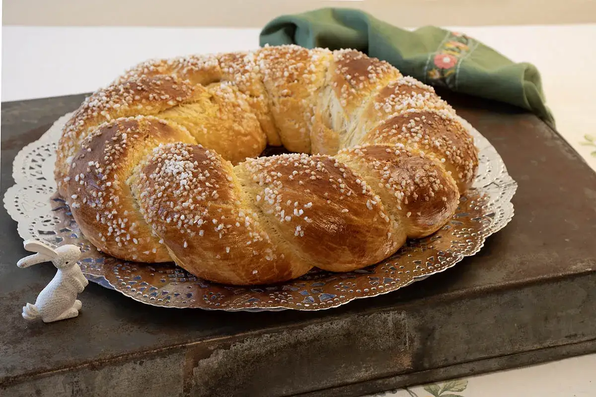 Una dorada rosca de Pascua, adornada con azúcar perlado, espera junto a un conejito blanco.