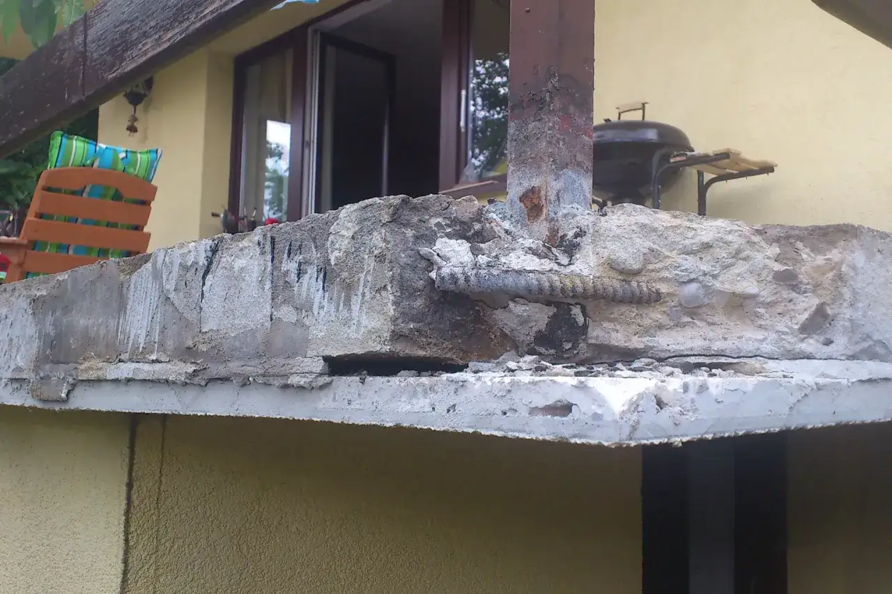 Uszkodzony beton na zewnątrz wymaga naprawy. Widoczne zbrojenie i ubytki świadczą o potrzebie prac.